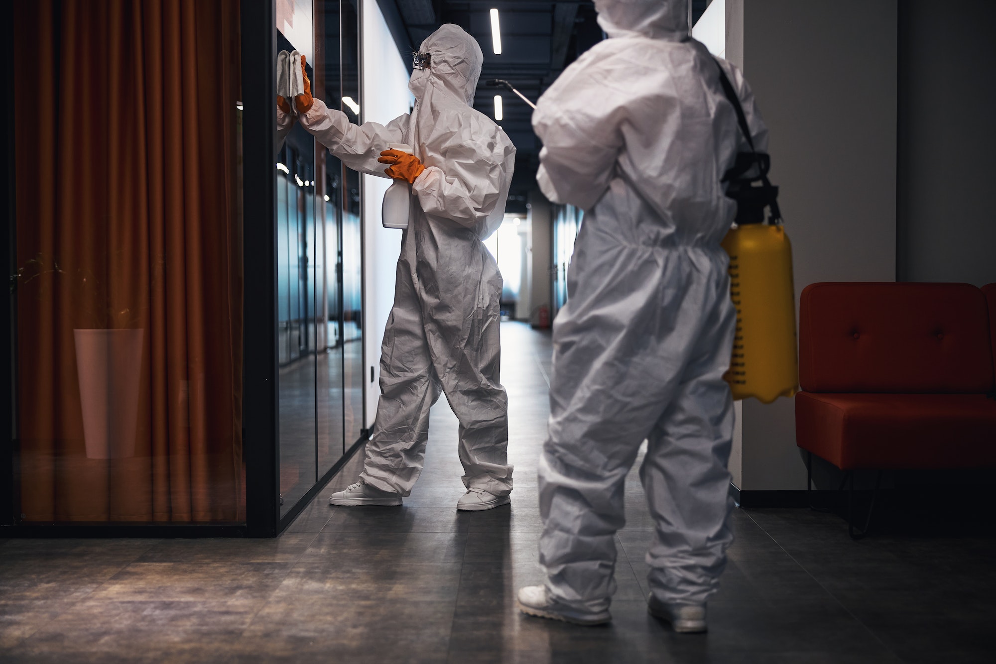 Two people in hazmat suits disinfecting the office corridor